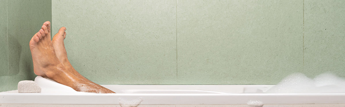 Person's feet in a bathtub with steam, against a green tiled wall.
